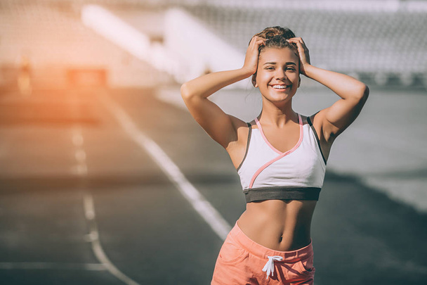 Elegant girl funny posing after training. Outdoor portrait of jocund young woman chilling at stadium. Grey background. sunshine background - 写真・画像
