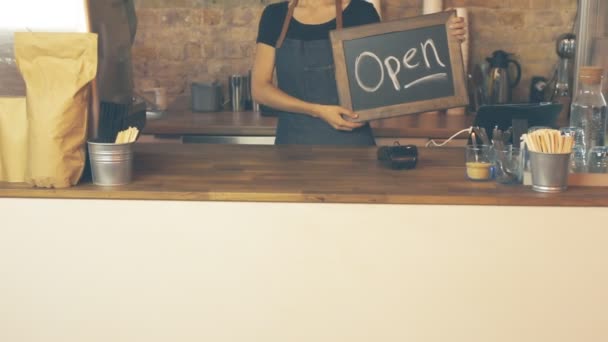 A coffee shop worker holds a Open sign and looks at the customer. - Video