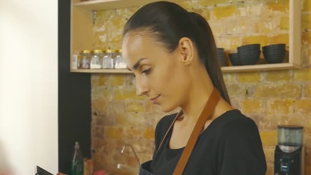 An attractive girl (the owner of a coffee house) works on a tablet. Slow motion. - Footage, Video