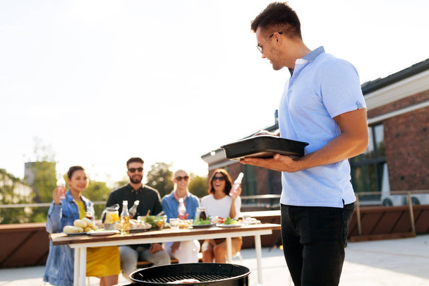 man cooking on bbq and friends at rooftop party - Foto, Imagem