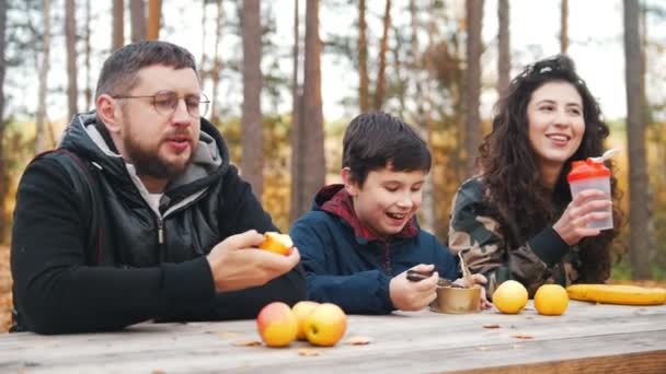 Familia feliz sentados uno al aire libre en el bosque en la mesa y disfrutar de la comida
. - Metraje, vídeo