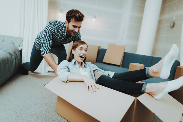 Young Couple Having Fun During Moving Into A New Apartment. Box Rolling Around The House. Holiday Leisure. Happy Family Weekend Joy. Love Each Other. Newlyweds In A New Housing. Relocation In Flat. - Photo, image