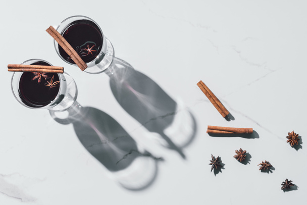 top view of glasses of mulled wine, cinnamon sticks and carnation on white tabletop - Foto, afbeelding