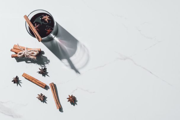 elevated view of mulled wine in glass and scattered cinnamon sticks on white tabletop - Fotoğraf, Görsel