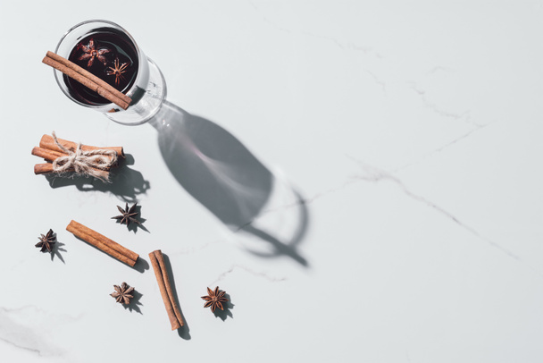 vista elevada de vidro de vinho ruminado, cravo e paus de canela em mesa branca
 - Foto, Imagem