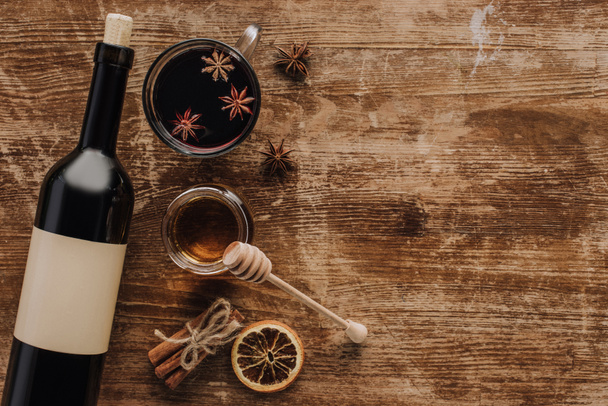 top view of mulled wine, honey and wine bottle on wooden table - Fotoğraf, Görsel