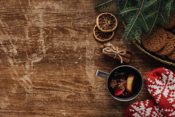 vista elevada de vino caliente en copa, manoplas y galletas sobre mesa de madera, concepto de Navidad
 - Foto, Imagen