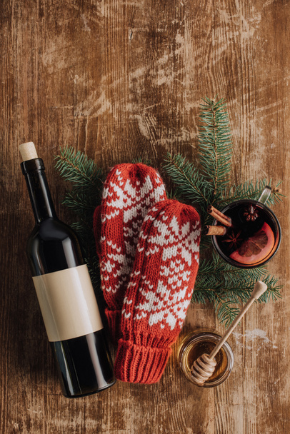 vista superior da garrafa de vinho, xícara de vinho quente e mitenes de inverno na mesa de madeira, conceito de natal
 - Foto, Imagem