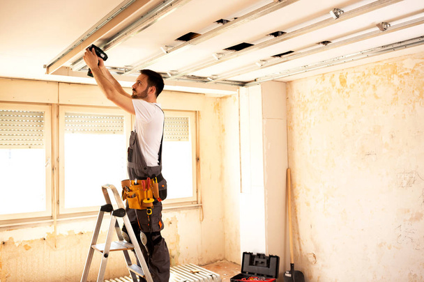 Crafty werknemer regelen van de juiste volgorde van de bouw van een plafond met behulp van een krachtige tool - Foto, afbeelding