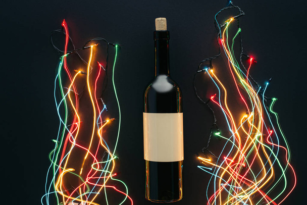 top view of wine bottle and garland lights with long exposure isolated on black, christmas concept - Photo, Image