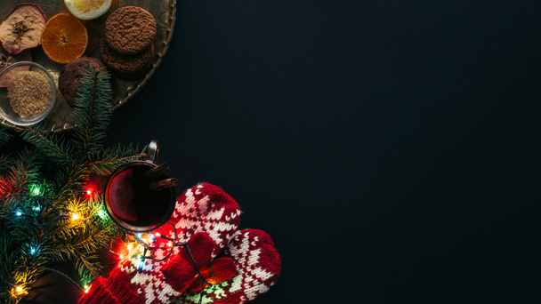 verhoogde weergave van kop glühwein, garland, wanten en cookies geïsoleerd op zwart, Kerstmis concept - Foto, afbeelding
