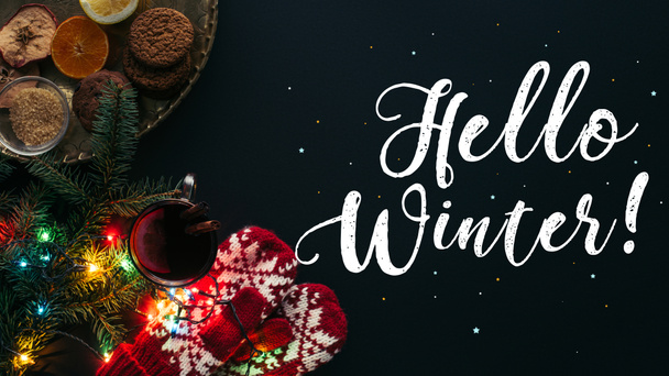 Вид сверху глинтвейна в чашке, гирлянде и приветствие Hello Winter isolated on black, christmas concept
 - Фото, изображение