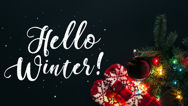 erhöhter Blick auf Glühwein in Tasse, Girlanden und Gruß Hallo Winter isoliert auf schwarz, Weihnachtskonzept - Foto, Bild