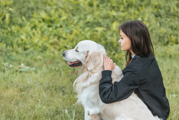 όμορφη νεαρή γυναίκα αγκαλιάζει σκυλί και κάθεται στο γρασίδι στο πάρκο - Φωτογραφία, εικόνα