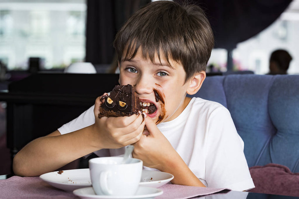 The boy is eating a large piece of cake in his hands  - Foto, Imagem
