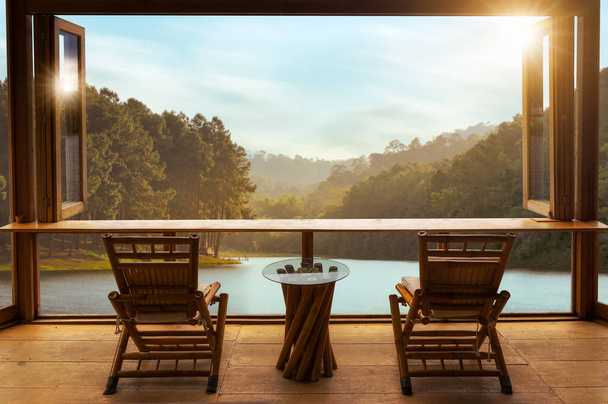 Beautiful landscape at cafe style minimal with wood tables and chairs on terrace against the outdoor lake view in cafe at sunrise. - Photo, Image
