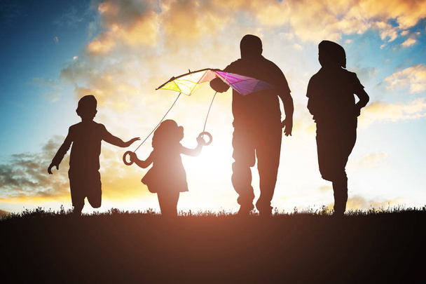 日没時にカラフルな凧を飛行しながら楽しんで家族のシルエット - 写真・画像