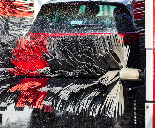 Black car in automatic car wash rotating red and black brush. Washing vehicle. - Photo, Image