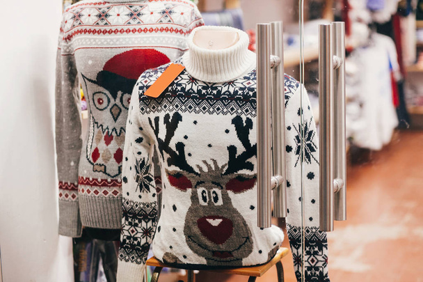 Suéteres de Navidad con renos y búho en el escaparate de tienda en la calle de la ciudad europea. Compras y ventas navideñas. Venta viernes negro. Decoraciones festivas
 - Foto, imagen