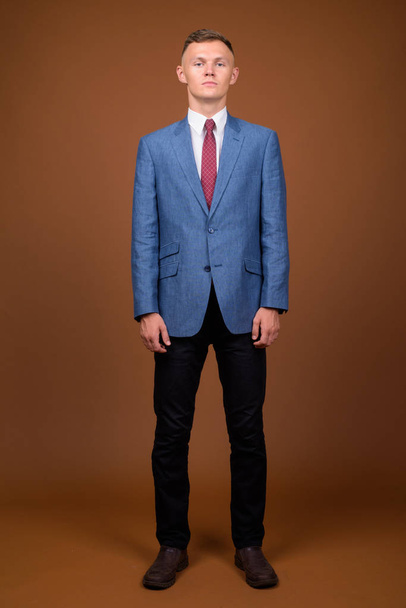 Νεαρός επιχειρηματίας φορώντας κοστούμι ενάντια σε καφέ φόντο - Φωτογραφία, εικόνα