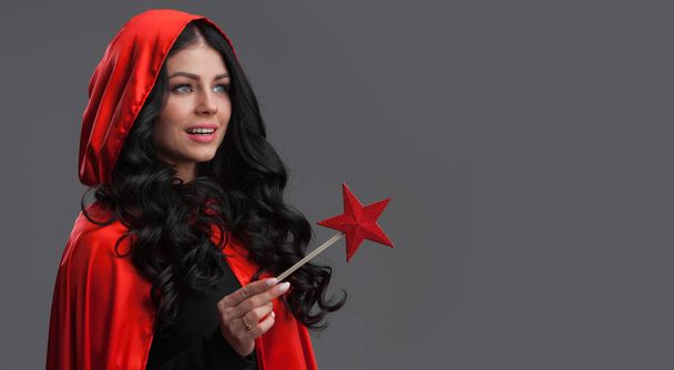 Woman in red cape with star shaped magic wand , gray background - Foto, Bild