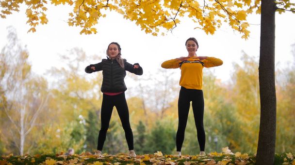 Chicas acrobáticas en chaquetas calentándose fuera antes de entrenar en el parque. Las manos a los lados
 - Foto, imagen