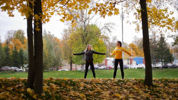 Akrobatische Mädchen wärmen sich draußen auf, bevor sie im Park trainieren. Hände zu den Seiten - Foto, Bild