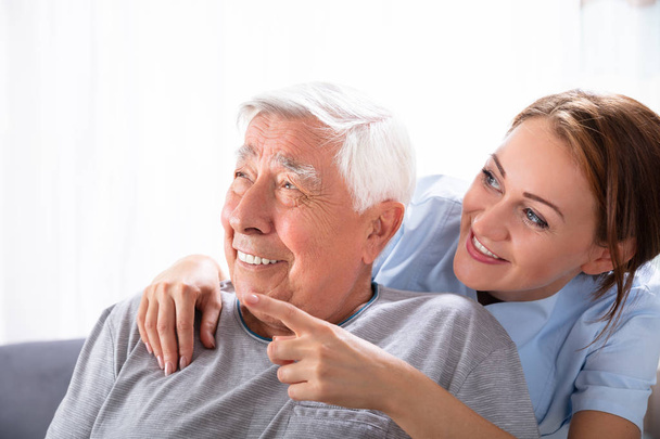 Close-up Of A Happy Female Nurse Pointing At Something To Senior Man - Foto, Imagen