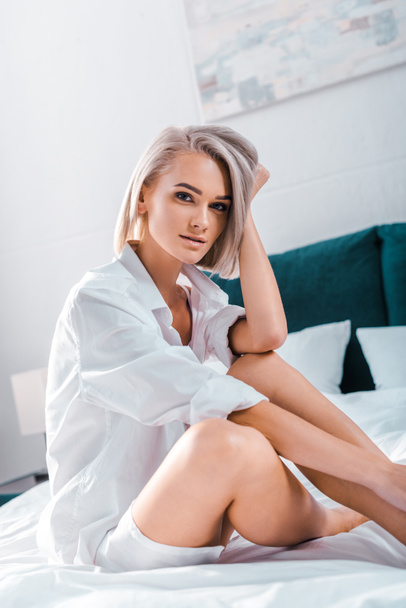 attractive young woman sitting on bed and looking at camera - Photo, Image