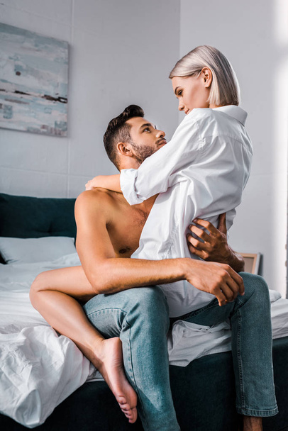 passionate young man sitting on bed with seductive girlfriend on top - Photo, Image