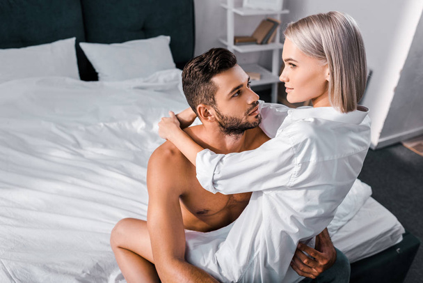 hoge hoekmening van mooie jonge vrouw zittend op vriendje in slaapkamer - Foto, afbeelding