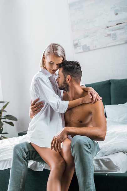 atractiva pareja joven abrazando mientras se sienta en la cama juntos
 - Foto, imagen