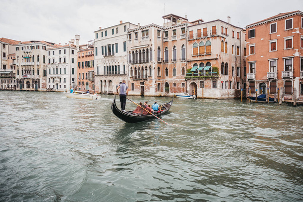 Wenecja, Włochy - 02 lipca 2017: Gondola na Canale Grande w Wenecji, z kolorowymi domami na tle. Łodzie są głównym środkiem transportu w mieście. - Zdjęcie, obraz