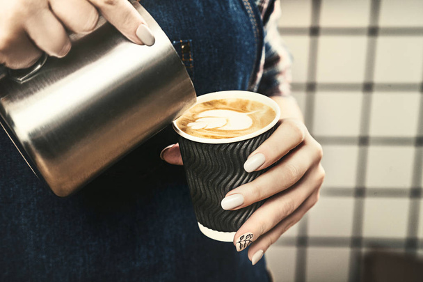 Cropped image of attractive female barista holds cup of latte at a scandinavian-style coffee shop. Professional Concept, copy space for logo, text, brand. Toned image. - 写真・画像