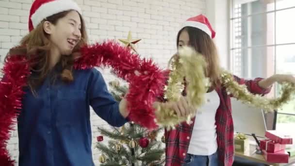 Slow motion - Happy Asian women celebrate christmas party with friends in office. Female celebrating New Year and Christmas Festival together. Group of beautiful people in Santa hats dance in office. - Footage, Video