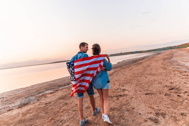 アメリカ人のカップルは、ビーチの上を歩くアメリカ国旗で覆われています。 - 写真・画像