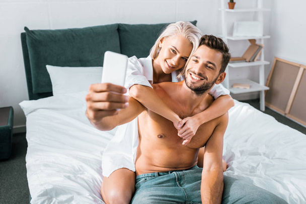happy young couple taking selfie together in bedroom - 写真・画像