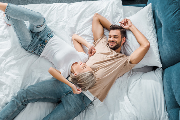 top view of young smiling couple lying on bed in bedroom - Foto, immagini