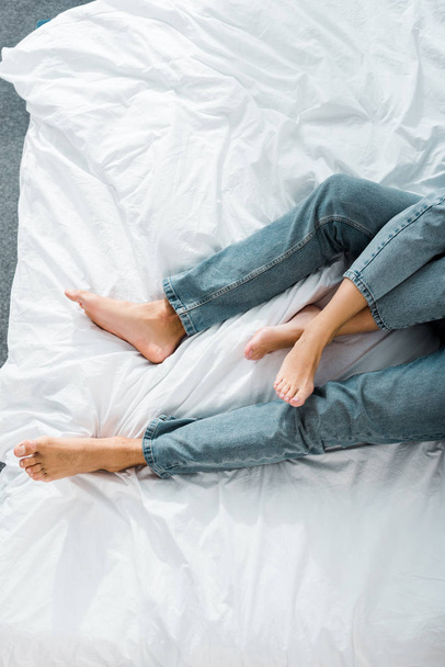 cropped image of young couple in jeans lying on bed in bedroom - Zdjęcie, obraz