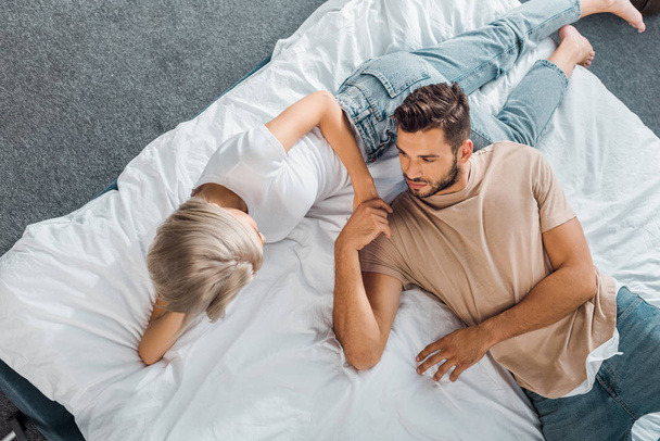 elevated view of young couple lying on bed and holding hands in bedroom - Foto, Bild