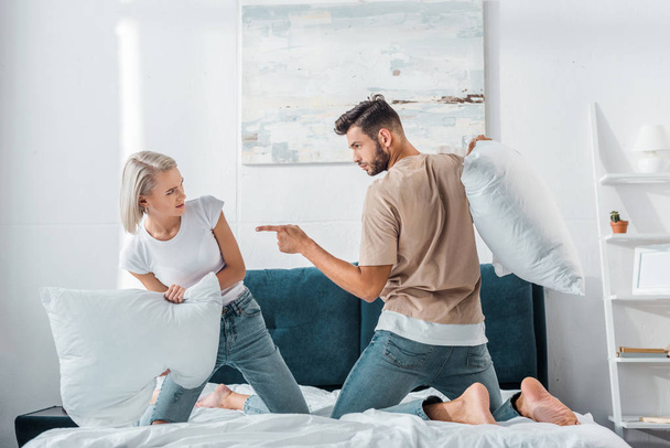 boyfriend pointing on girlfriend during fight with pillows on bed in bedroom - Foto, Bild