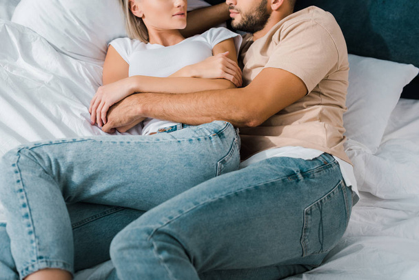 обрезанный образ молодой пары, обнимающейся на кровати в спальне
 - Фото, изображение