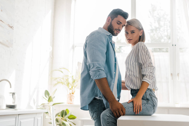 side view of passionate young couple hugging in kitchen, girlfriend looking at camera - Foto, Bild