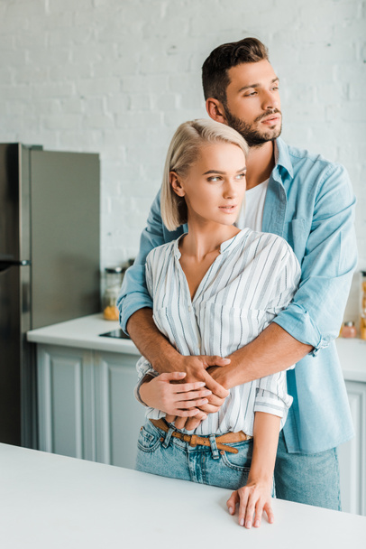handsome boyfriend hugging girlfriend from back in kitchen and they looking away - Photo, Image