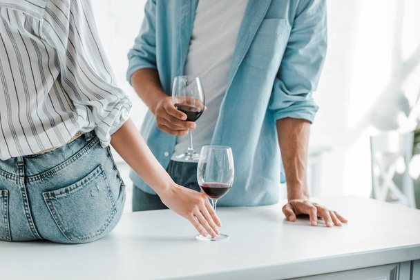 cropped image of couple with glasses of red wine in kitchen - Fotografie, Obrázek