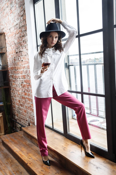 Fashion portrait of beauty brunette model wearing white shirt and pink pants. Young beautiful woman posing in luxury apartments interior - Photo, Image