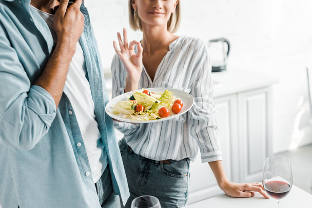 cropped image of girlfriend showing okay gesture to salad in kitchen - Foto, imagen