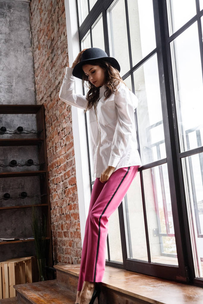 Fashion portrait of beauty brunette model wearing white shirt and pink pants. Young beautiful woman posing in luxury apartments interior - Foto, Bild