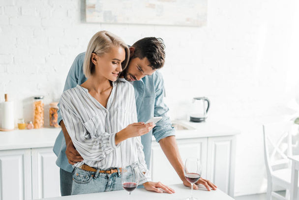 young couple looking at smartphone together in kitchen - Foto, immagini