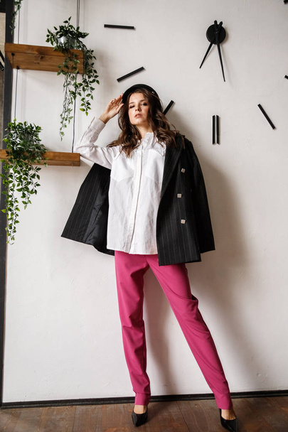 Retrato de moda de modelo morena de belleza con chaqueta negra, camisa blanca y pantalones rosados. Joven hermosa mujer posando en apartamentos de lujo interior
 - Foto, imagen
